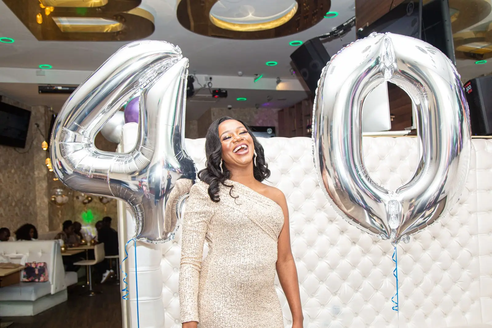 Woman celebrating her 40th birthday beside large silver number balloons at a birthday party venue